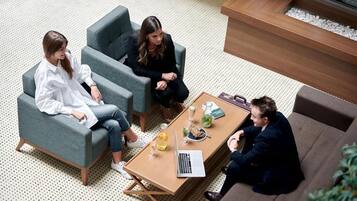 Un ambiente interior moderno con tres personas sentadas alrededor de una mesa, una computadora portátil, bebidas y un menú.