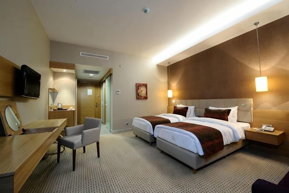 Habitación de hotel con cama, mesita de noche, lámpara, televisor y escritorio con silla.