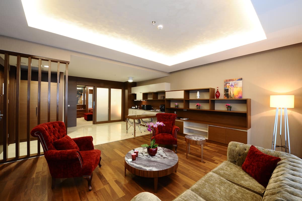 A modern living room with a wooden floor, a round coffee table with a vase, red chairs, a beige sofa, and a dining area in the background.
