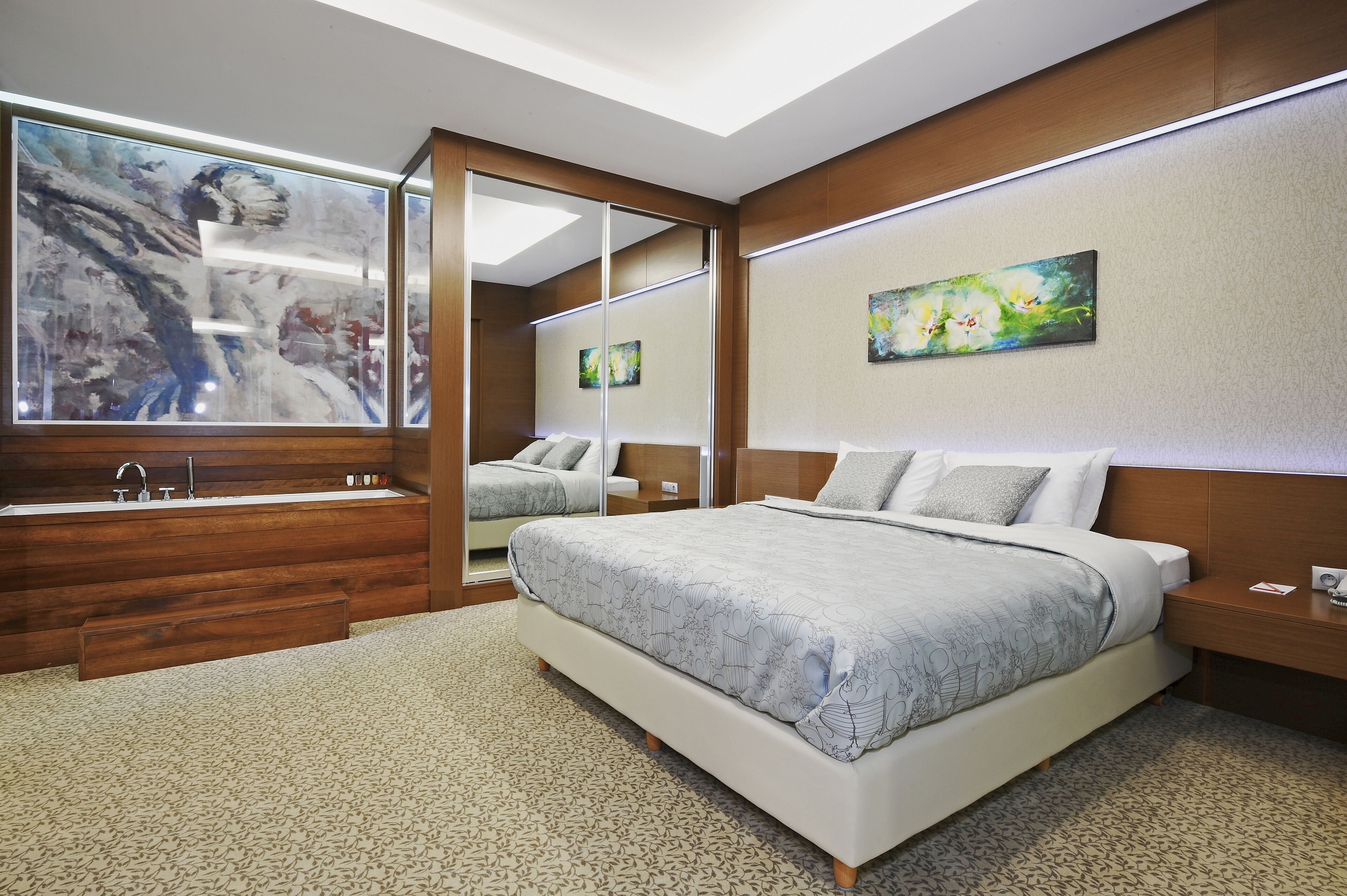 Un dormitorio moderno con una cama grande, una bañera integrada y un espejo amplio.