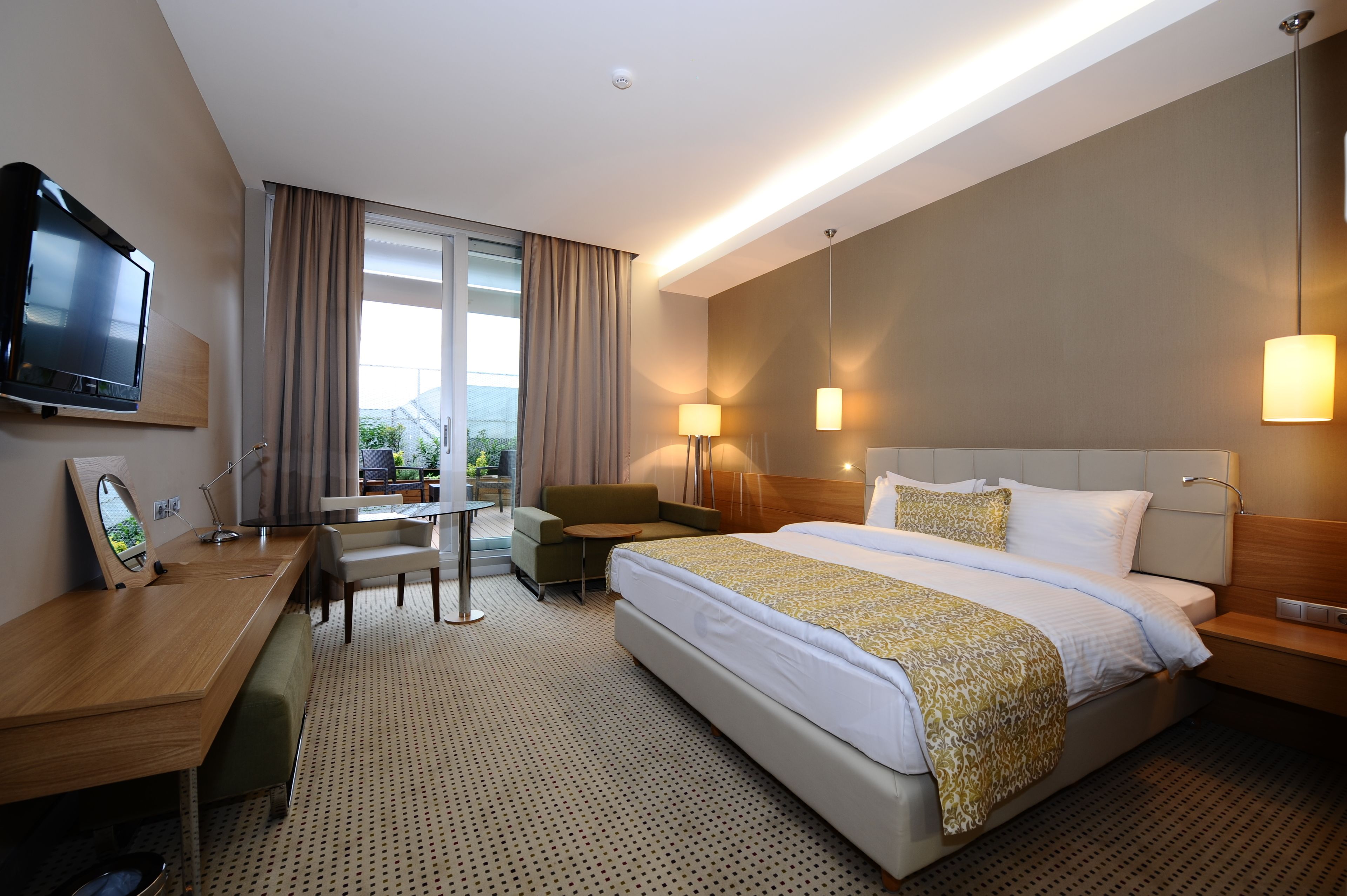 A hotel room with a bed, desk, chair, TV, and lamps.