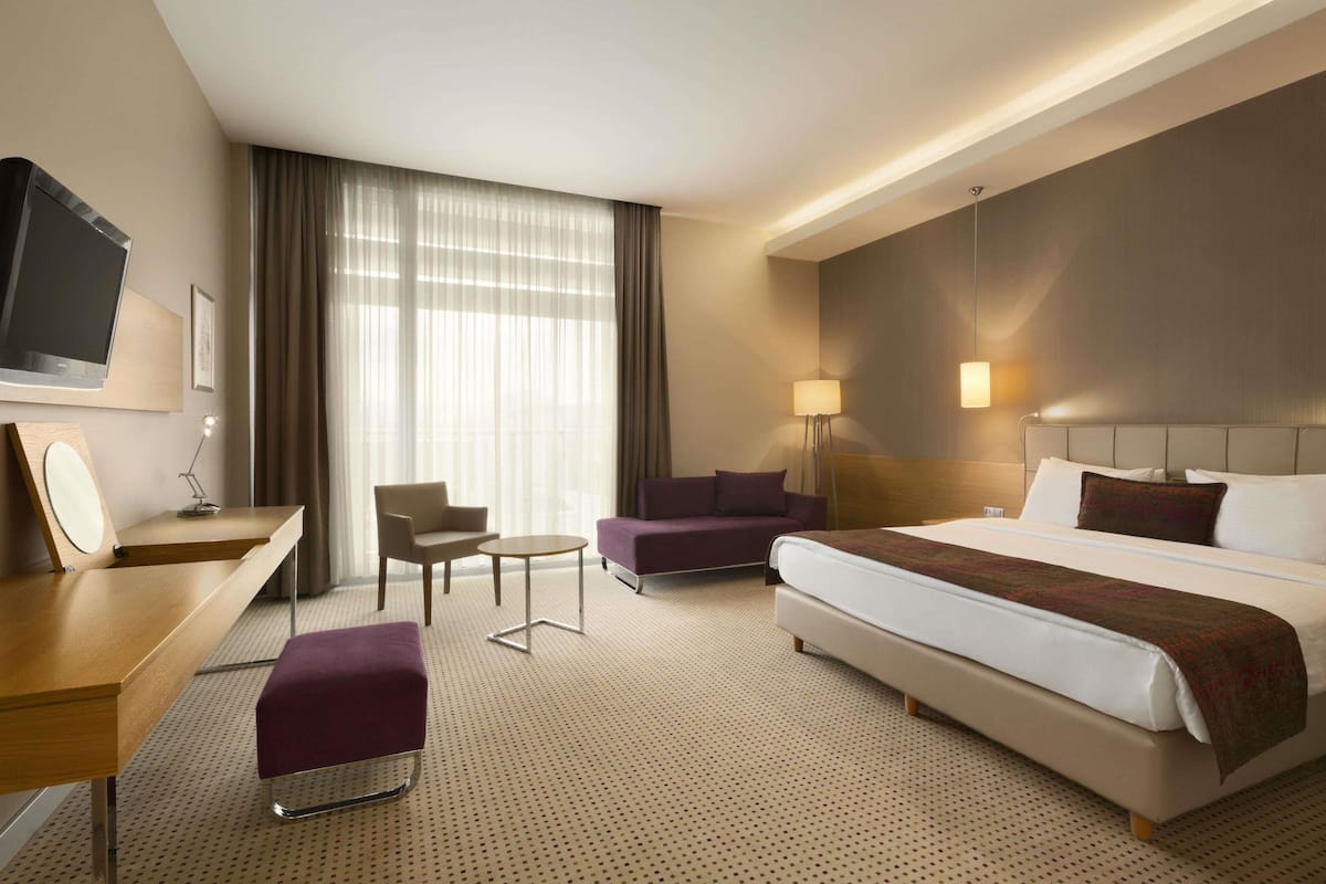 A hotel room with a large bed, a desk, a chair, a sofa, and a TV.