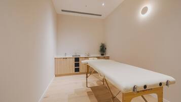 A clinical examination room with a wooden cabinet, a white examination table, and a small potted plant.