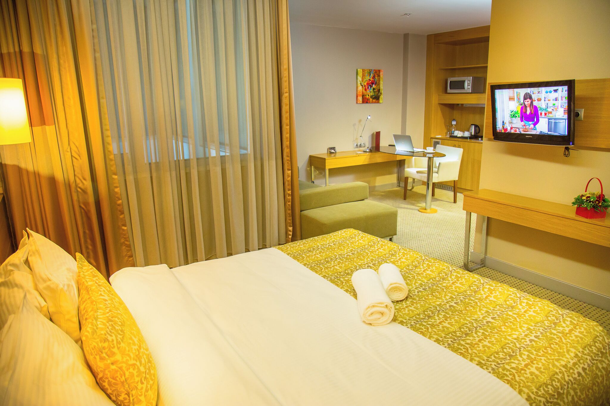 A hotel room with a bed, a desk, a television, and a window with curtains.