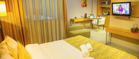 A hotel room with a bed, a desk, a television, and a window with curtains.