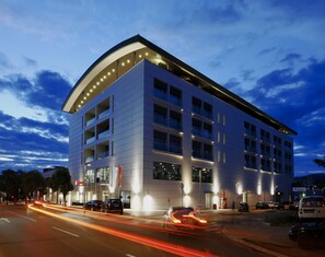 A modern multi-story building with a curved roofline, large windows, and a well-lit facade. - Ramada by Wyndham Podgorica (Podgorica)