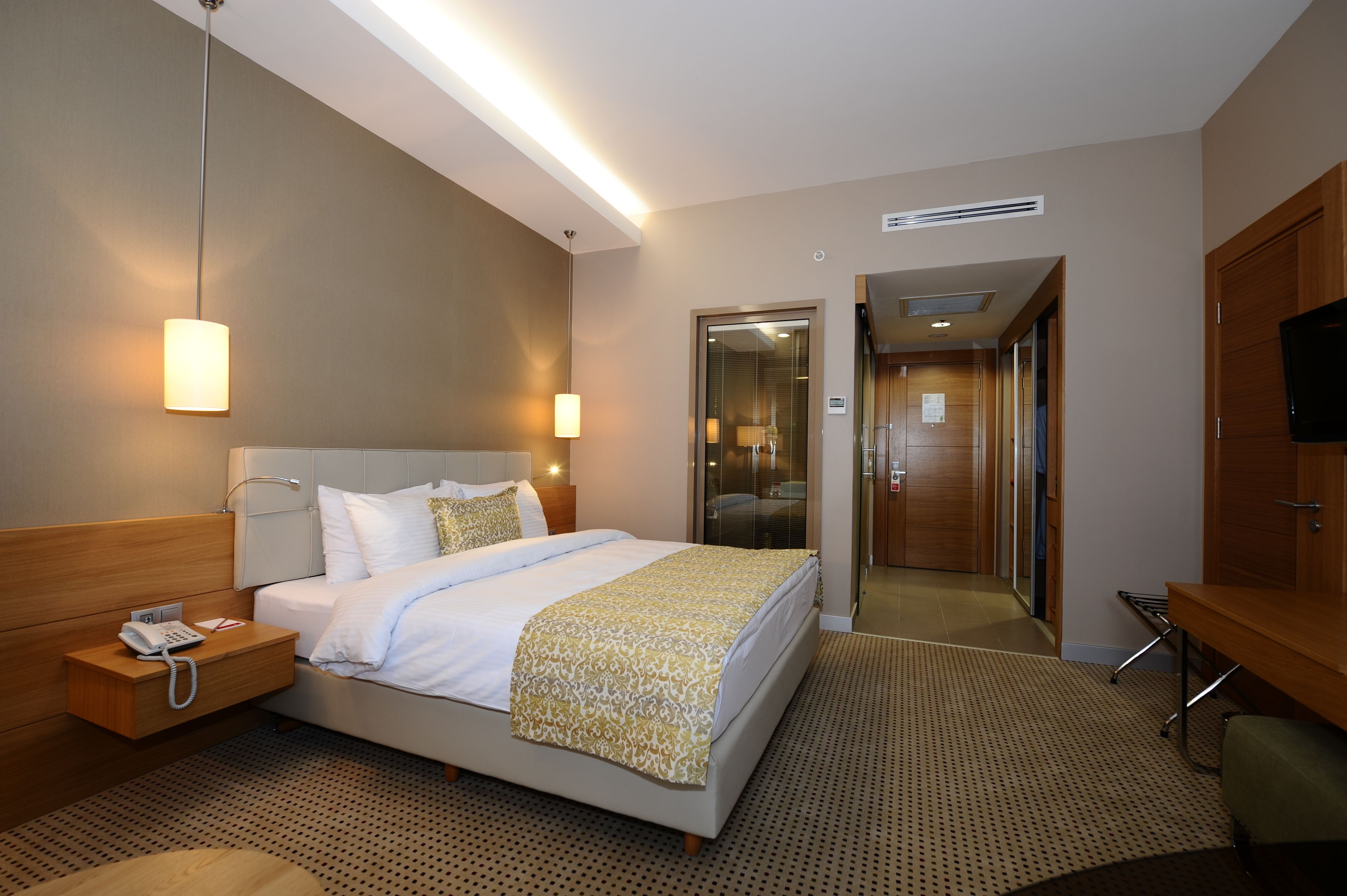 A hotel room with a bed, bedside table with a phone, a lamp, and a TV on a wooden cabinet.