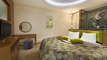 A modern hotel room with a large bed, a television, a desk, and a ceiling light fixture.
