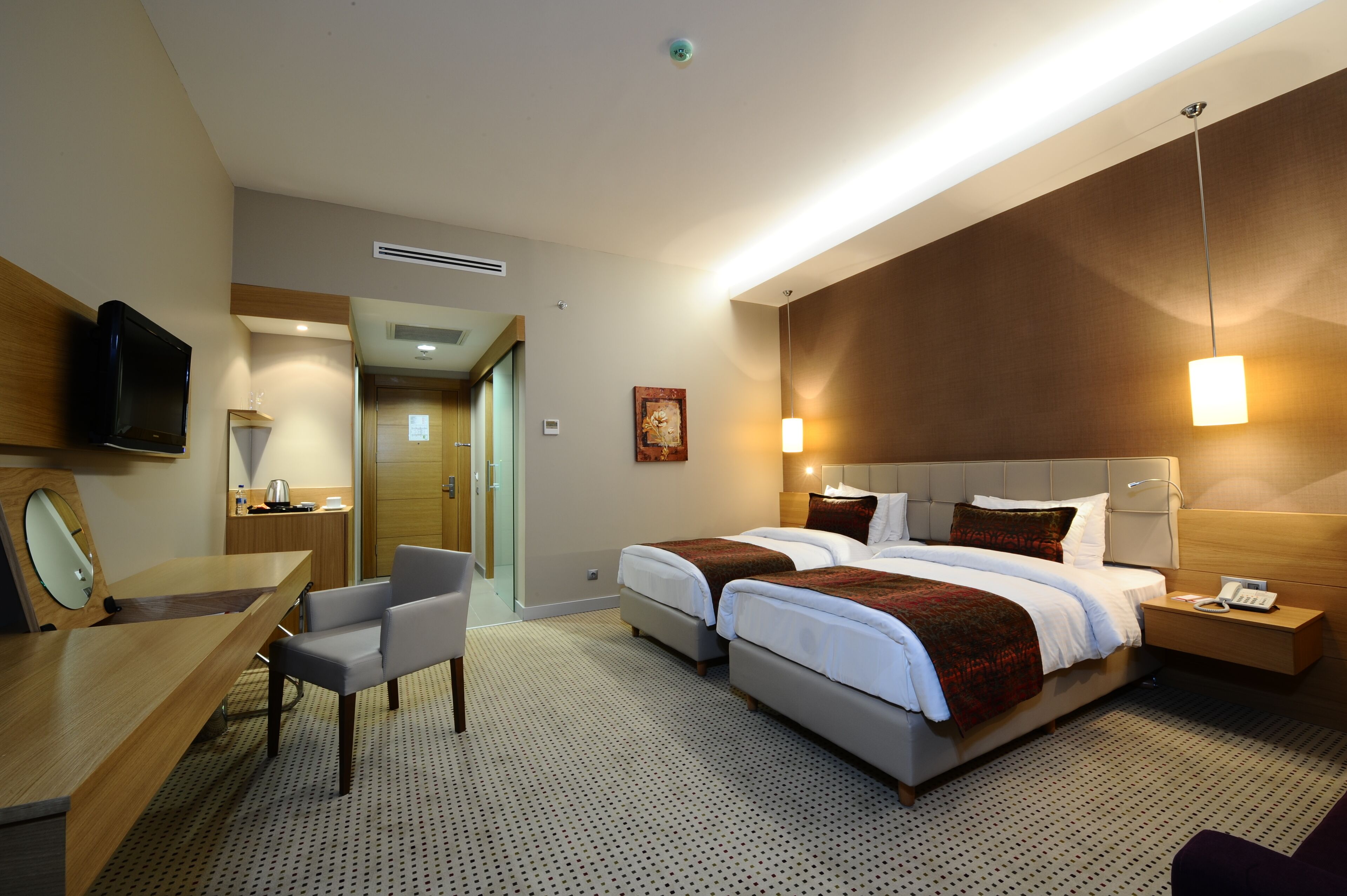 A hotel room with two beds, a desk, a chair, a TV, and a bathroom visible through an open door.