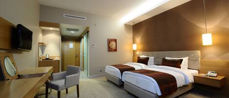 A hotel room with two beds, a desk, a chair, a TV, and a bathroom visible through an open door.