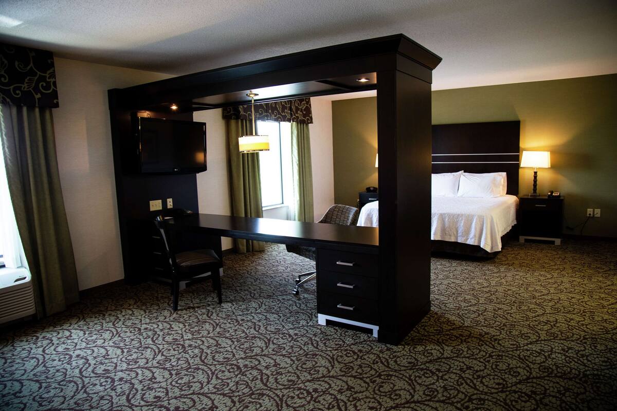 Quarto de hotel com escrivaninha, cama, televisão e abajur.