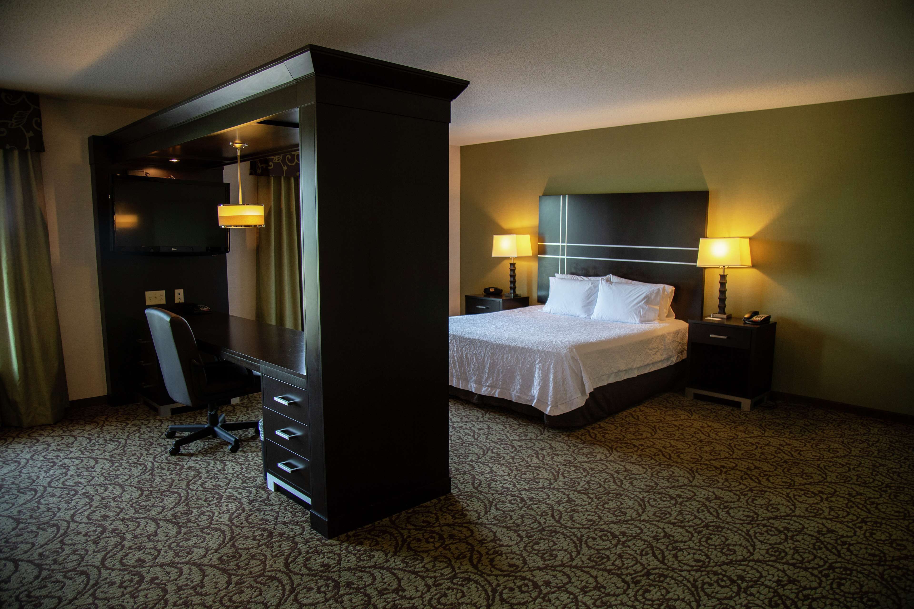 A hotel room with a large bed, two bedside tables with lamps, a desk with a chair, and a television on a stand.
