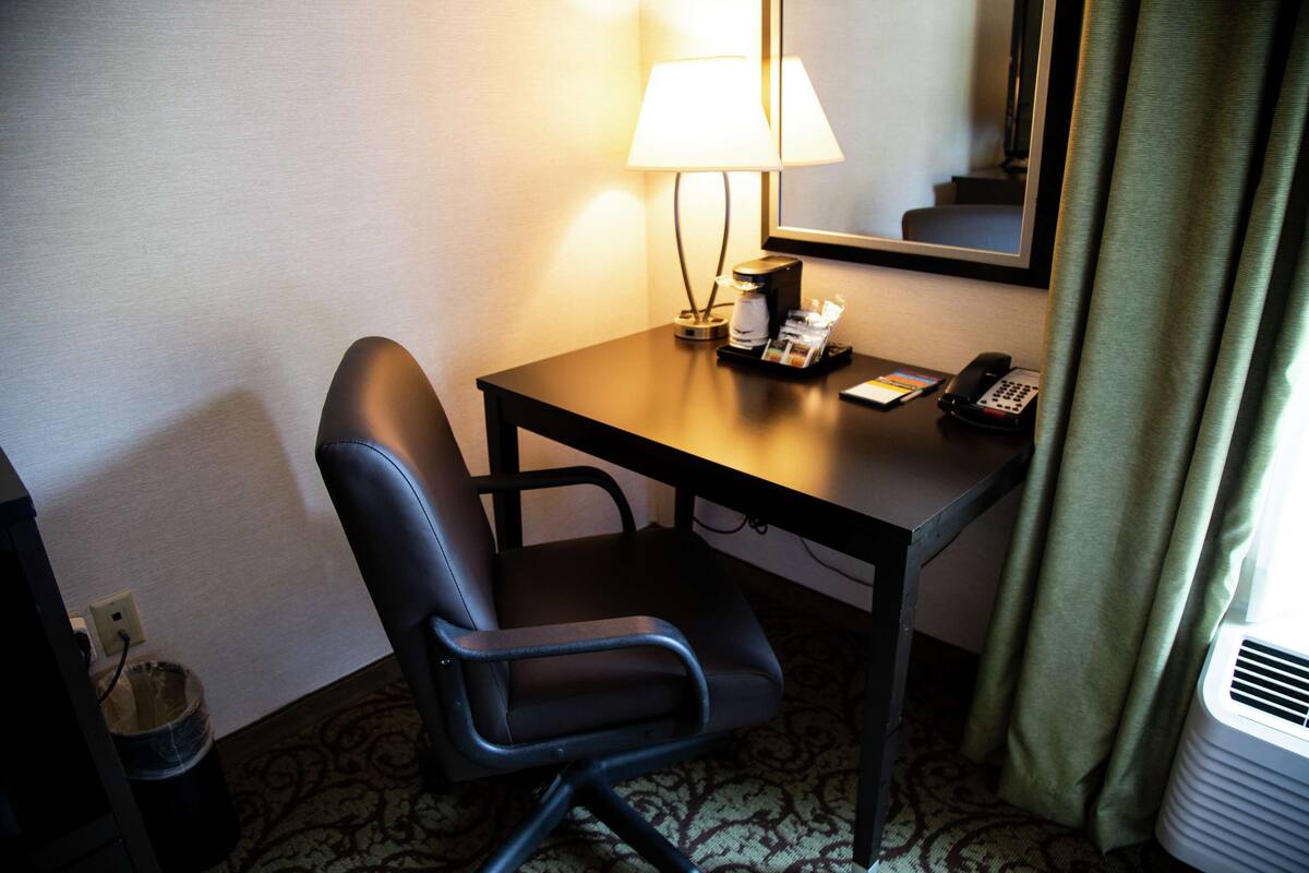 Quarto de hotel com escrivaninha, cadeira, abajur, telefone e aparelho de ar condicionado.