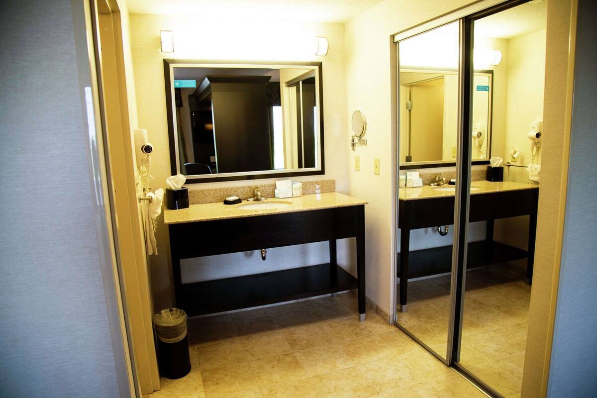 Casa de banho de hotel com duas pias, um espelho e um lixo.
