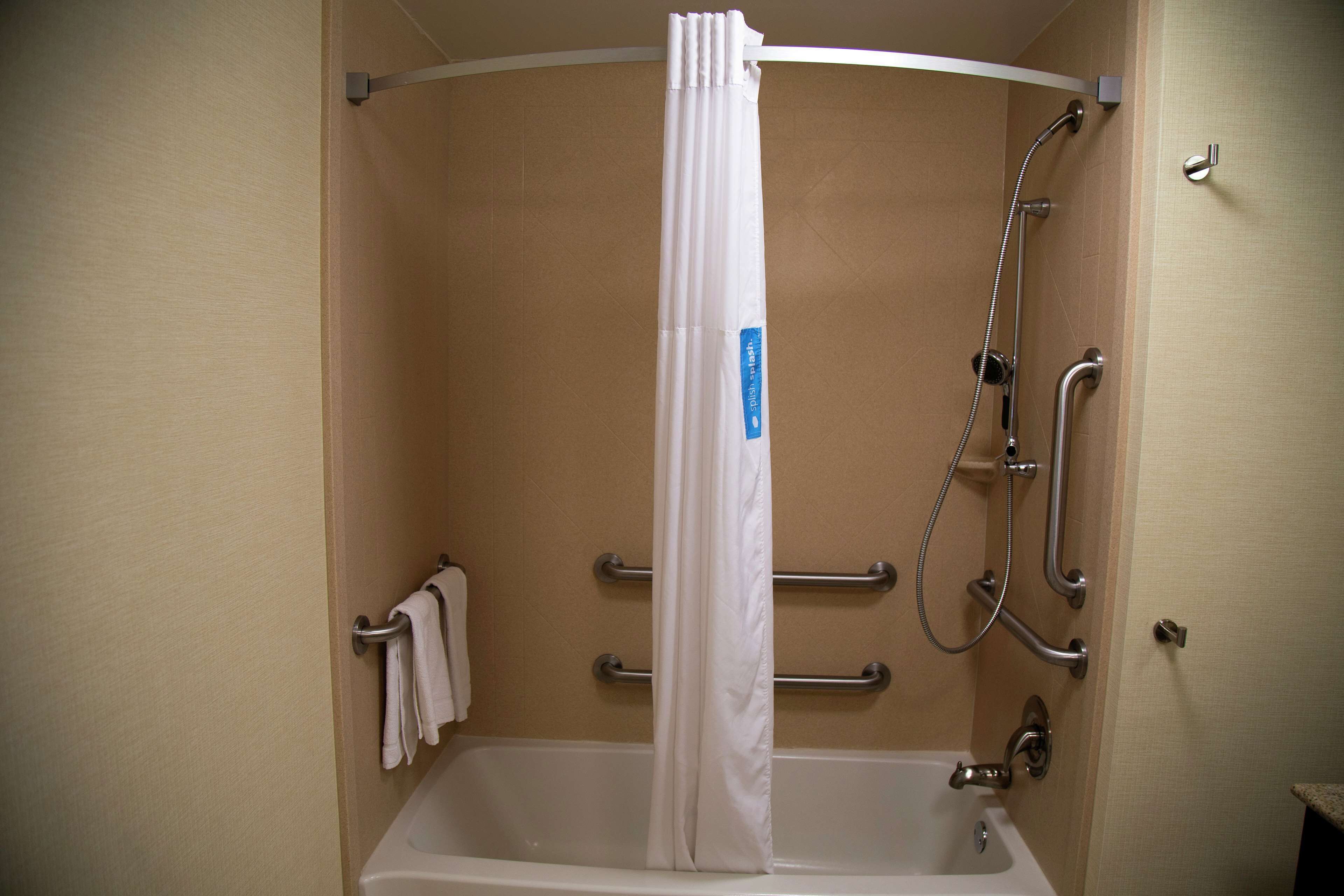 A standard shower stall with a white curtain, grab bars, and a handheld showerhead.