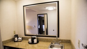 Ein Hotelbad mit einer Granitplatte, einem Waschbecken, einem Spiegel und einer Kaffeemaschine.