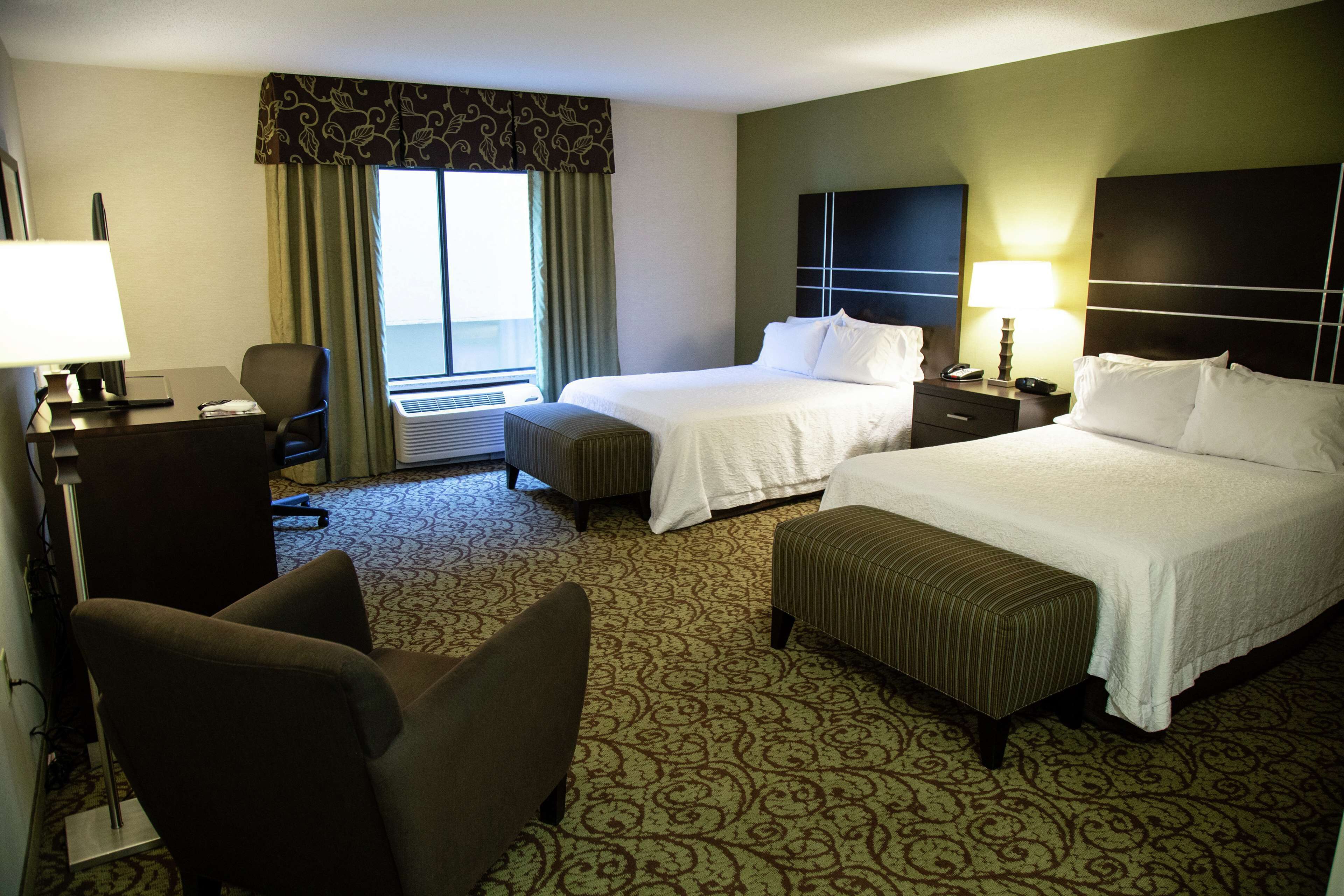 A hotel room with two beds, a desk, a chair, and a window with curtains.