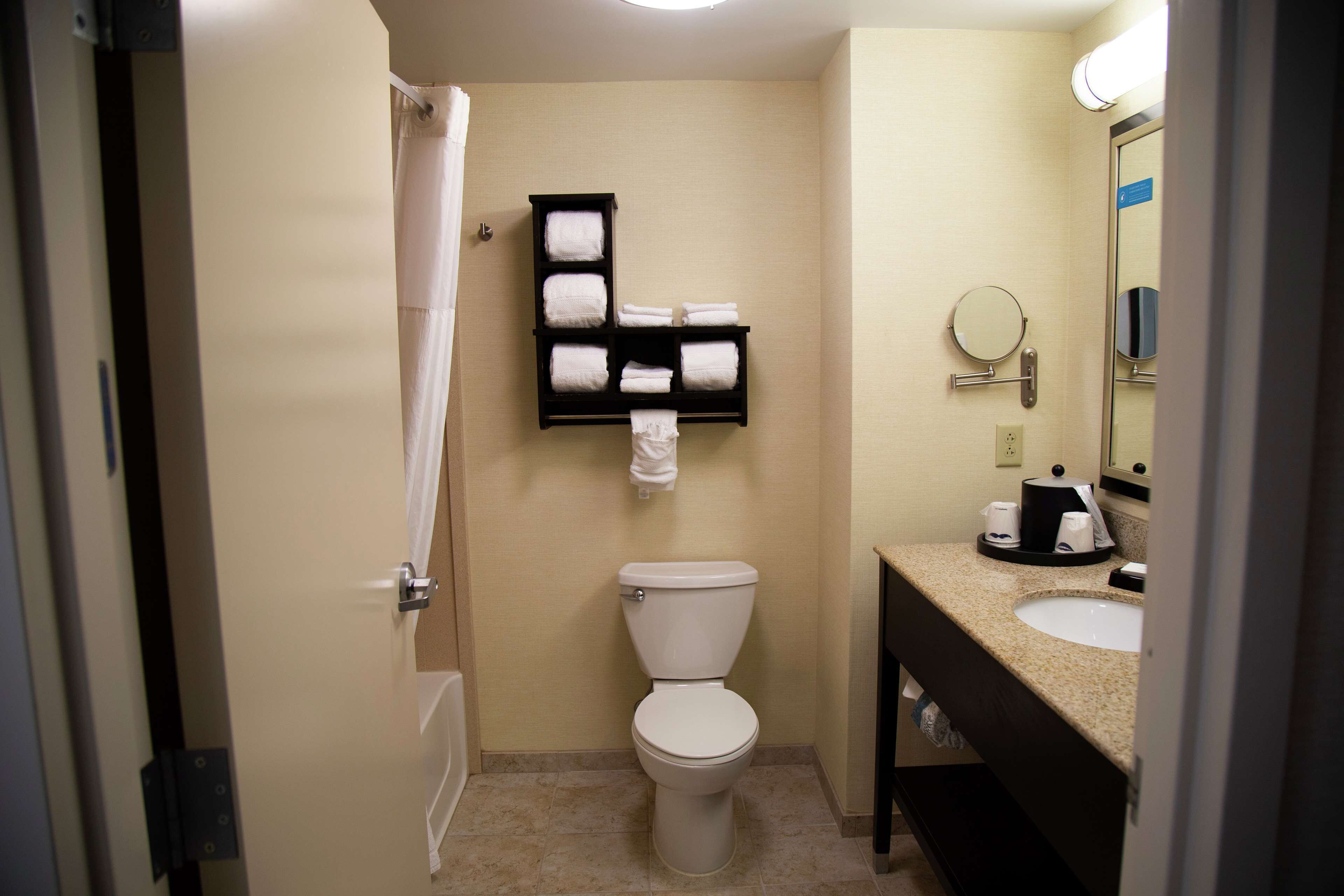 Ein kleines Hotelbad mit Toilette, Waschbecken, Handtuchhalter mit mehreren Handtüchern und Spiegel.