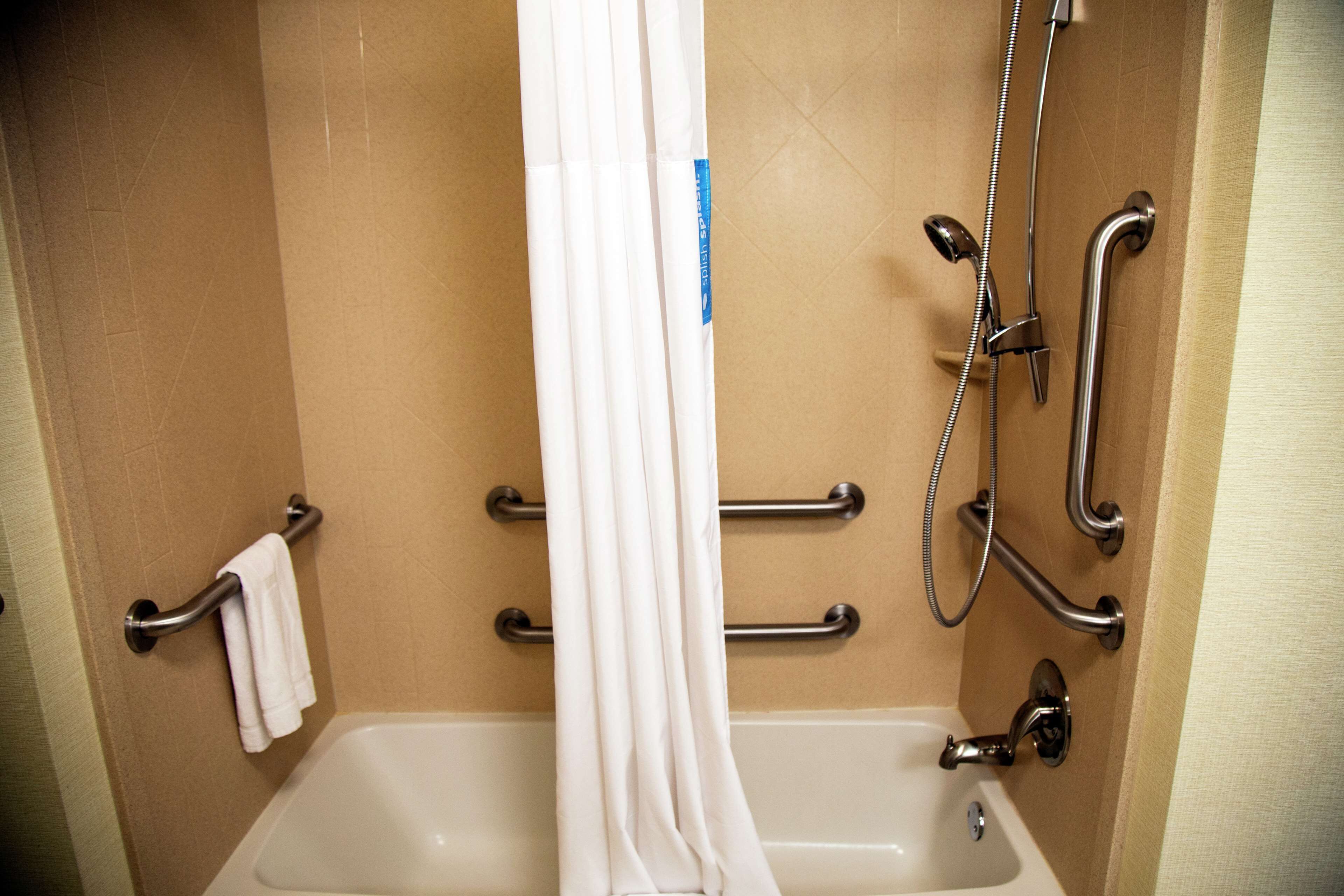 Un baño con bañera, barras de apoyo y cabezal de ducha.