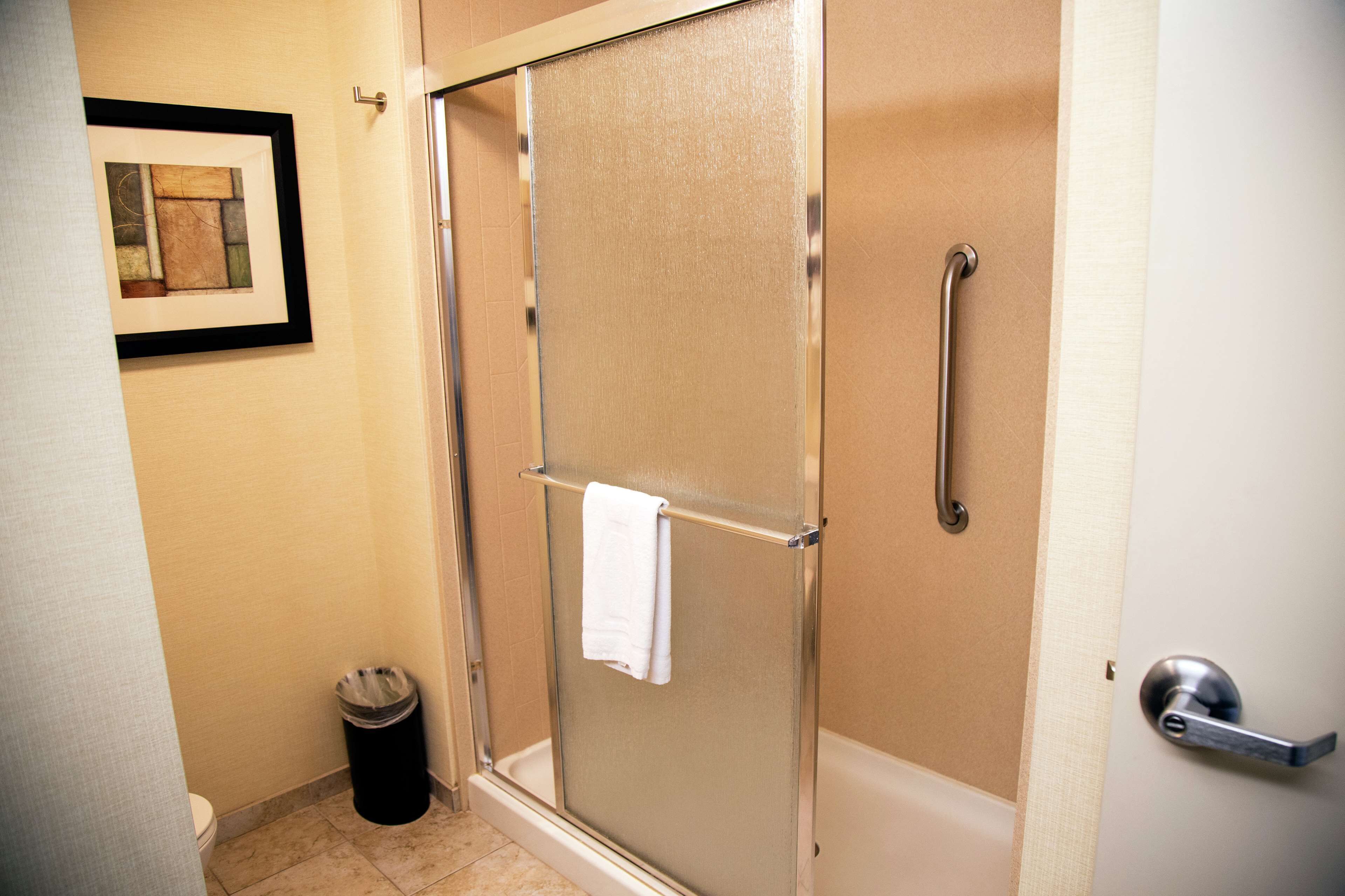 A shower with a glass door, a towel hanging on the door handle, and a trash can in the corner.