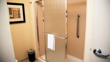 A shower with a glass door, a towel hanging on the door handle, and a trash can in the corner.