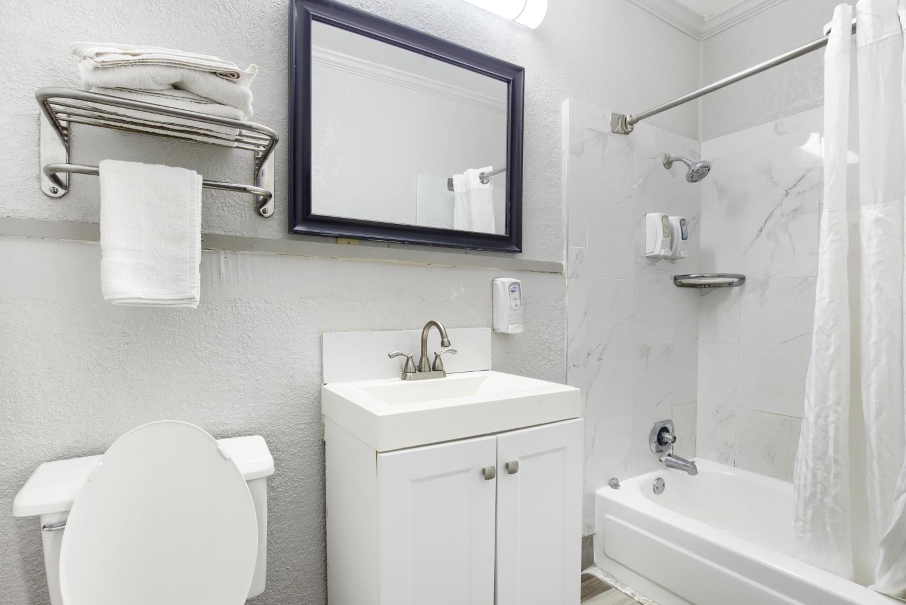 A modern bathroom with a toilet, sink, mirror, towel rack, and shower.