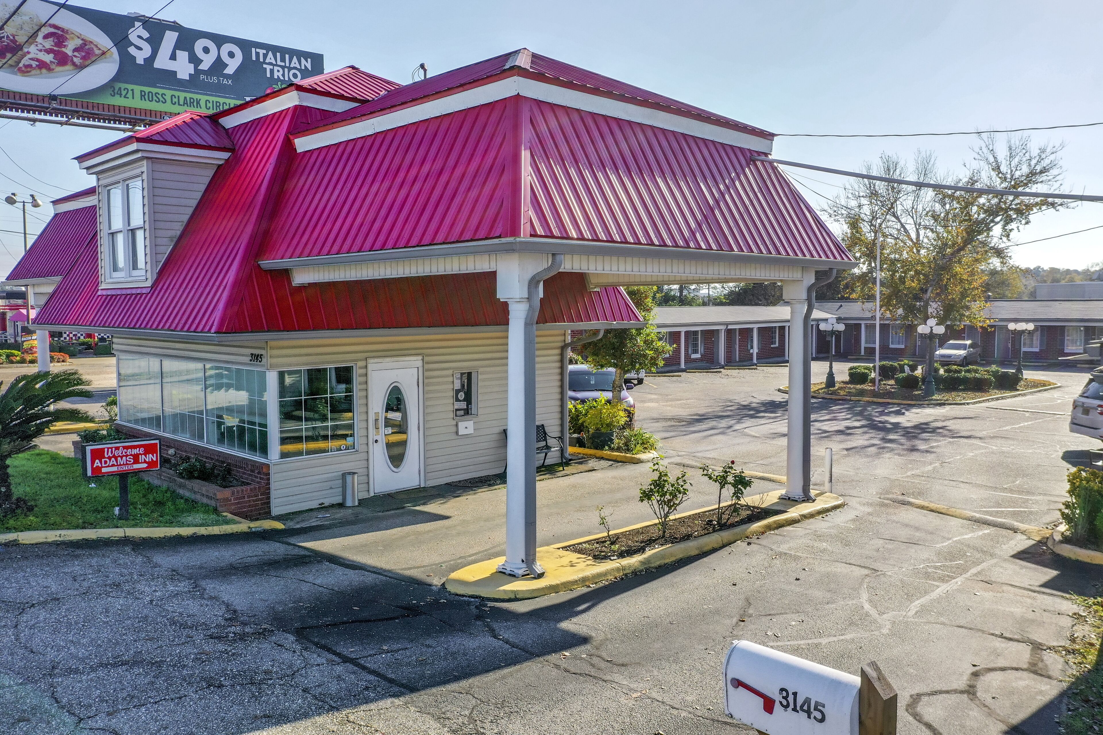 A motel with a red roof, a sign for Italian Trio, and a welcome sign for Adams Inn.