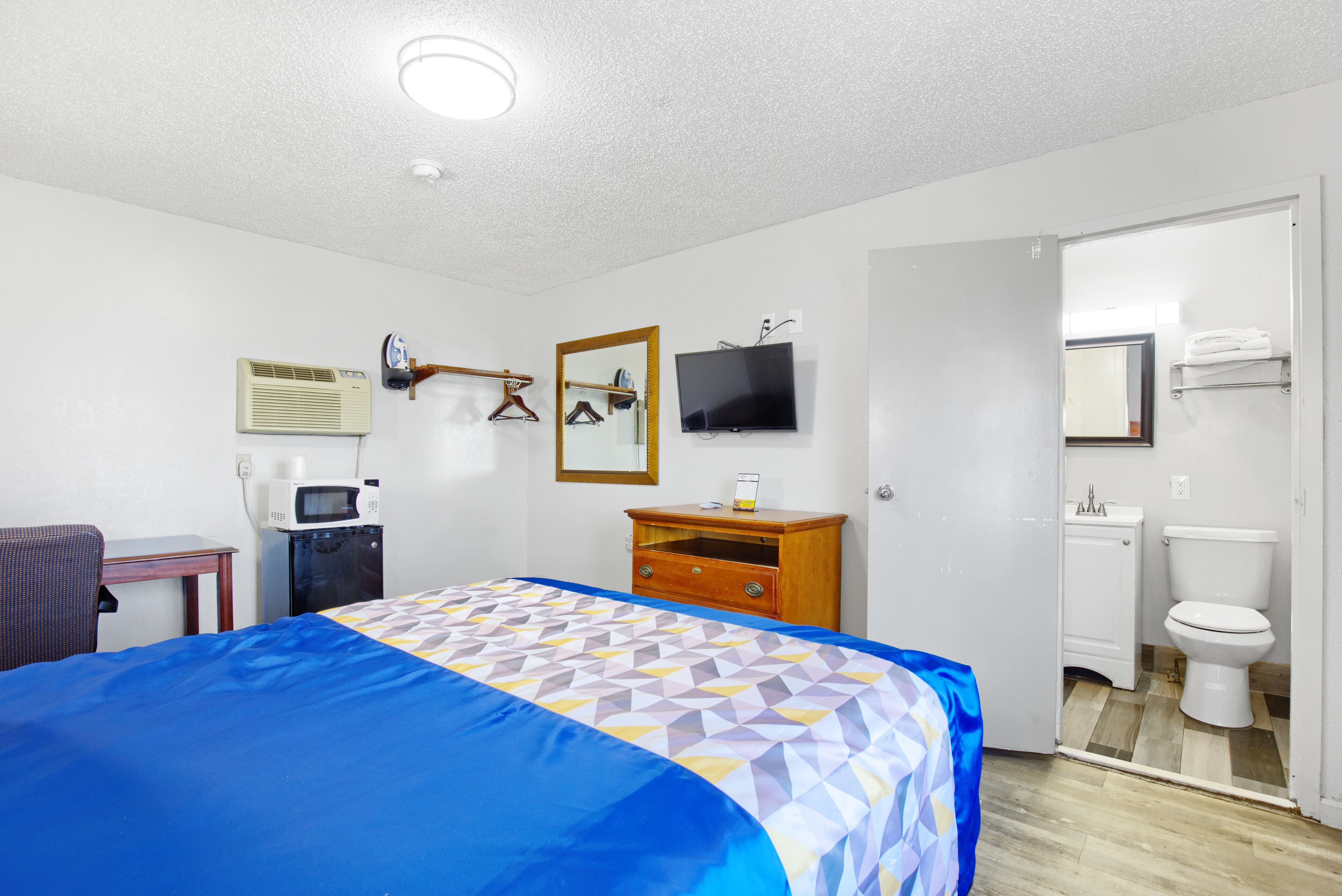 A hotel room with a bed, a desk, a microwave, a TV, a mirror, and a bathroom.