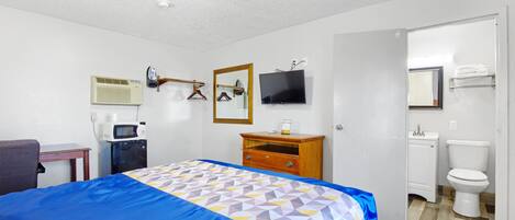 Ein Hotelzimmer mit einem Bett, einem Schreibtisch, einer Mikrowelle, einem Fernseher, einem Spiegel und einem Badezimmer.