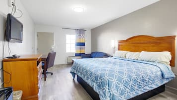 Un dormitorio con cama, cómoda de madera, escritorio y televisor en la pared.
