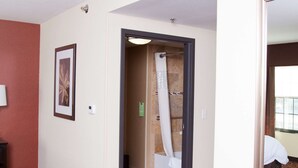 Un pasillo de hotel con alfombra estampada, un cuadro enmarcado en la pared y un espejo que refleja una habitación.