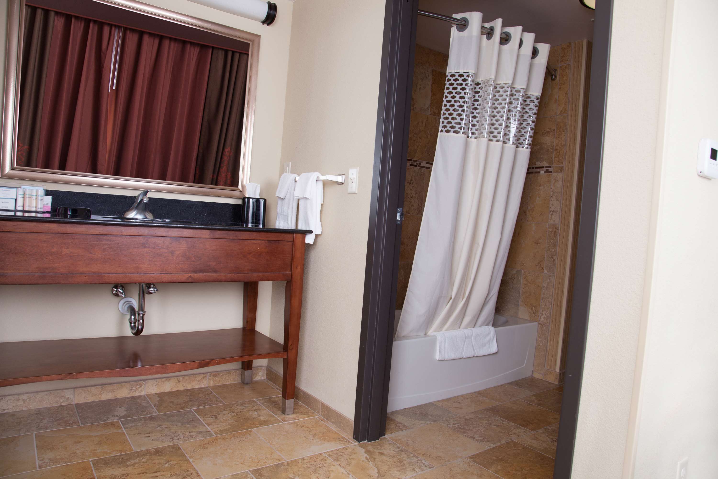 Un baño con tocador de madera, un espejo, cortina de ducha y bañera.