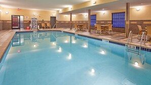 Zona de piscina de hotel con piscina cristalina, sillas de descanso y un área de estar con mesas y sillas.