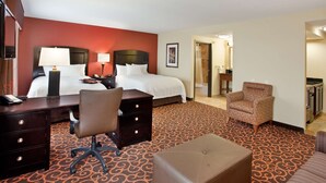 Habitación de hotel con cama, escritorio, silla, reposapiés y baño visible a través de una puerta abierta.