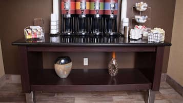 A coffee station with multiple coffee dispensers, a small vase, and a basket of snacks.