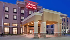 Un hotel Hampton Inn & Suites con fachada de piedra, varias ventanas y una entrada bien iluminada.