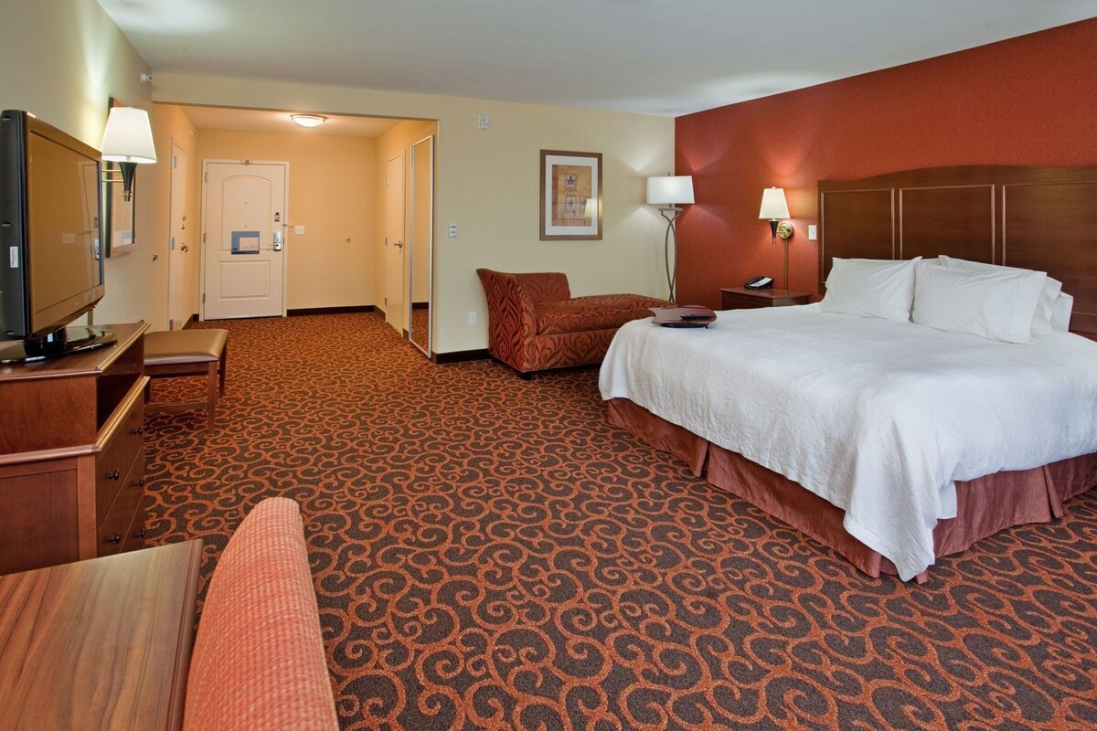 Ein Hotelzimmer mit Bett, Schreibtisch mit Fernseher, Sessel, Sofa und Teppichboden.