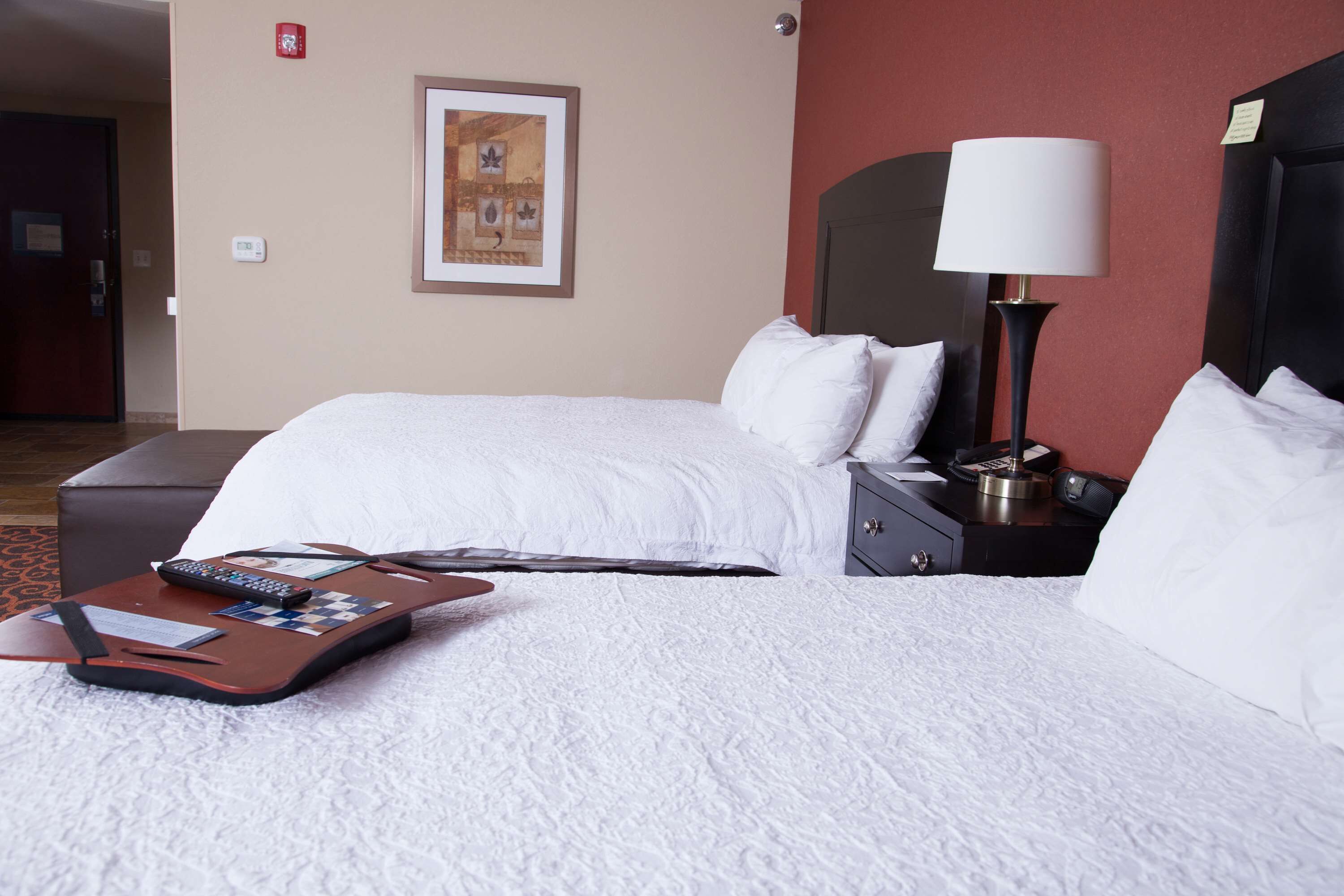 A hotel room with a bed, a nightstand, a lamp, and a suitcase.
