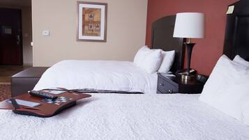 A hotel room with a bed, a nightstand, a lamp, and a suitcase.