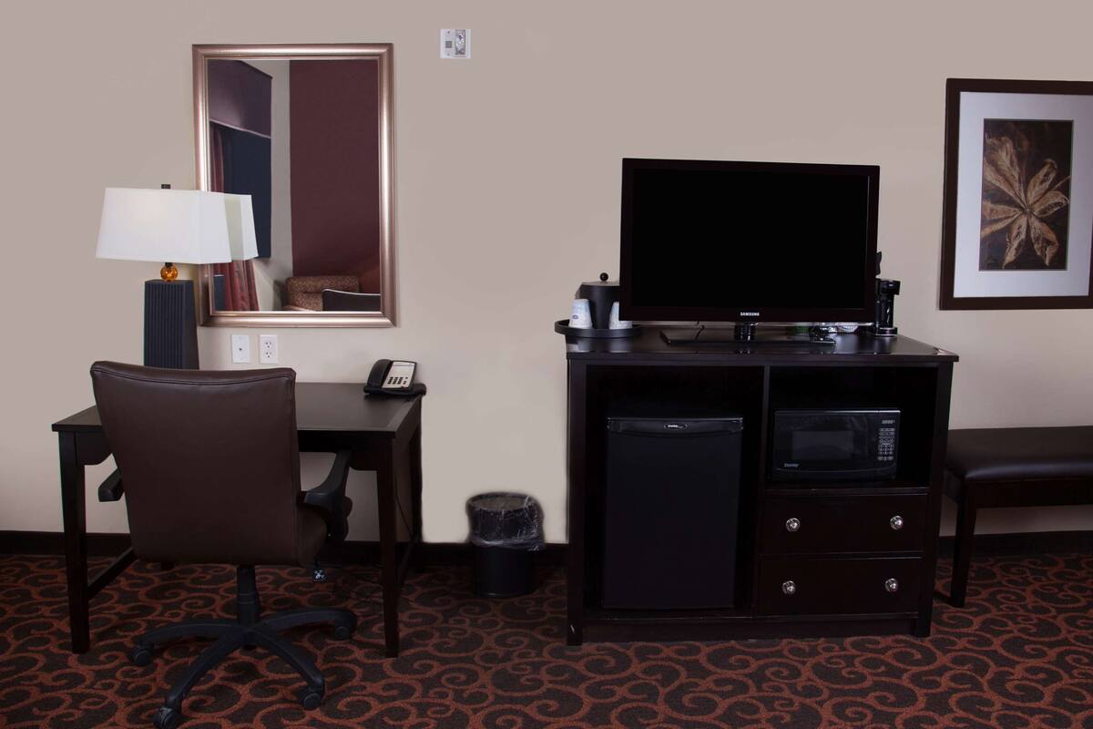 Habitación de hotel con escritorio, silla, televisor y un pequeño armario.