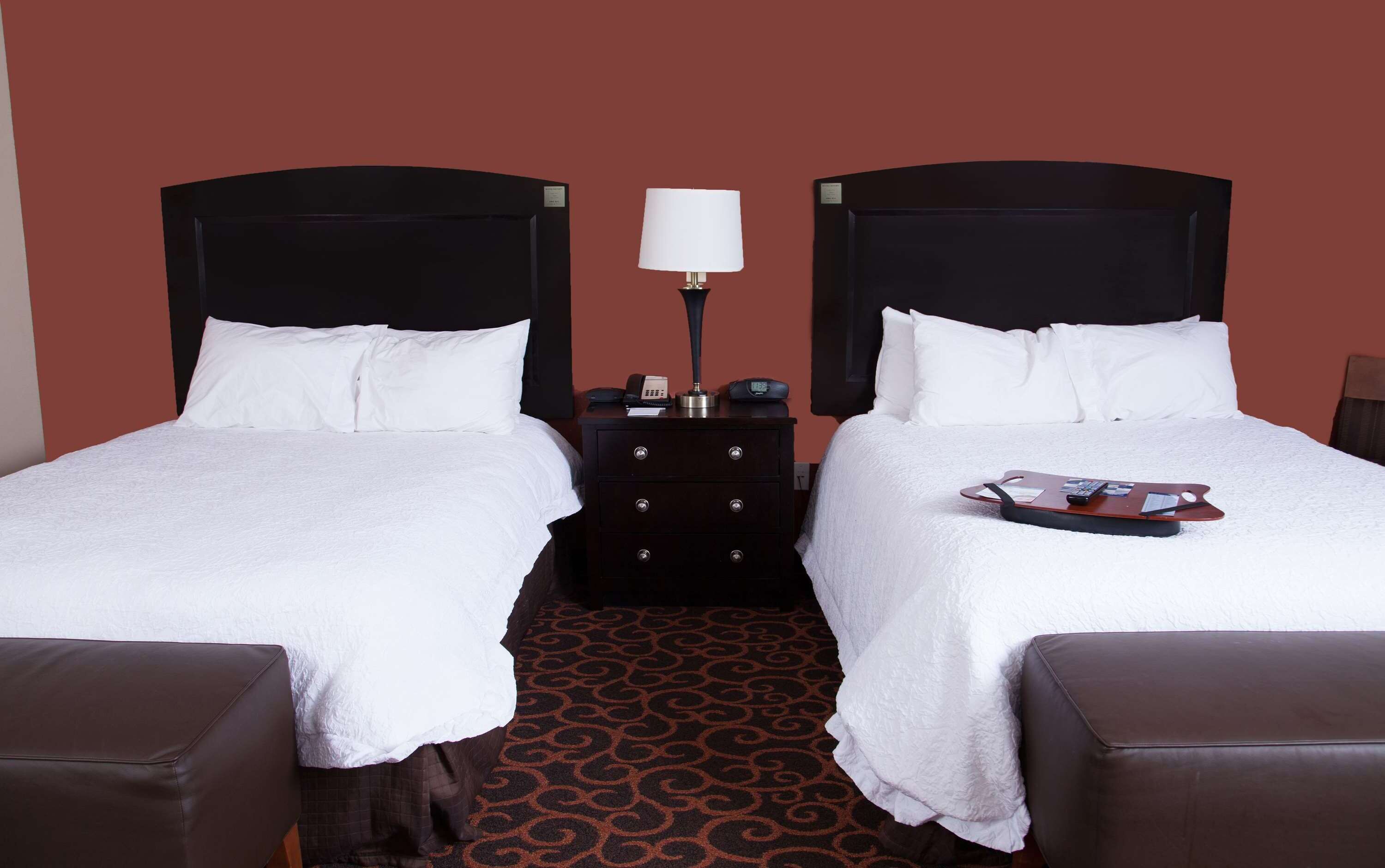A hotel room with two beds, a nightstand with a lamp, and a magazine on the right bed.