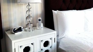 A neatly made bed with white linens, a white bedside table with a lamp, and a telephone. - The Milestone Inn (Woodbury)