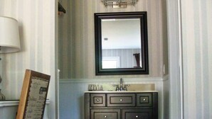 A hotel bathroom with a large mirror, a vanity with drawers, a sink, and a towel rack. - The Milestone Inn (Woodbury)
