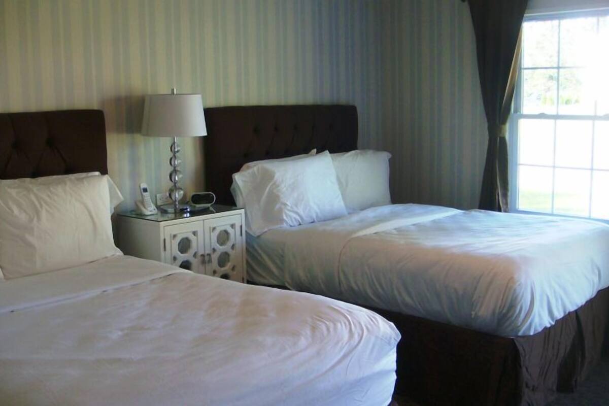 A hotel room with two beds, a nightstand with a lamp, and a window with curtains.