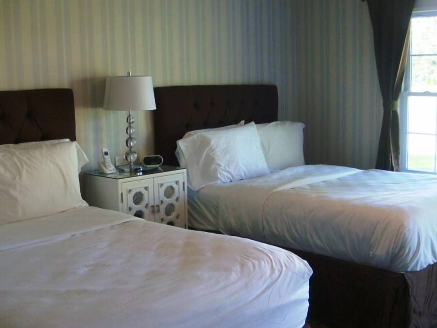 A hotel room with two beds, a nightstand with a lamp, and a window with curtains.