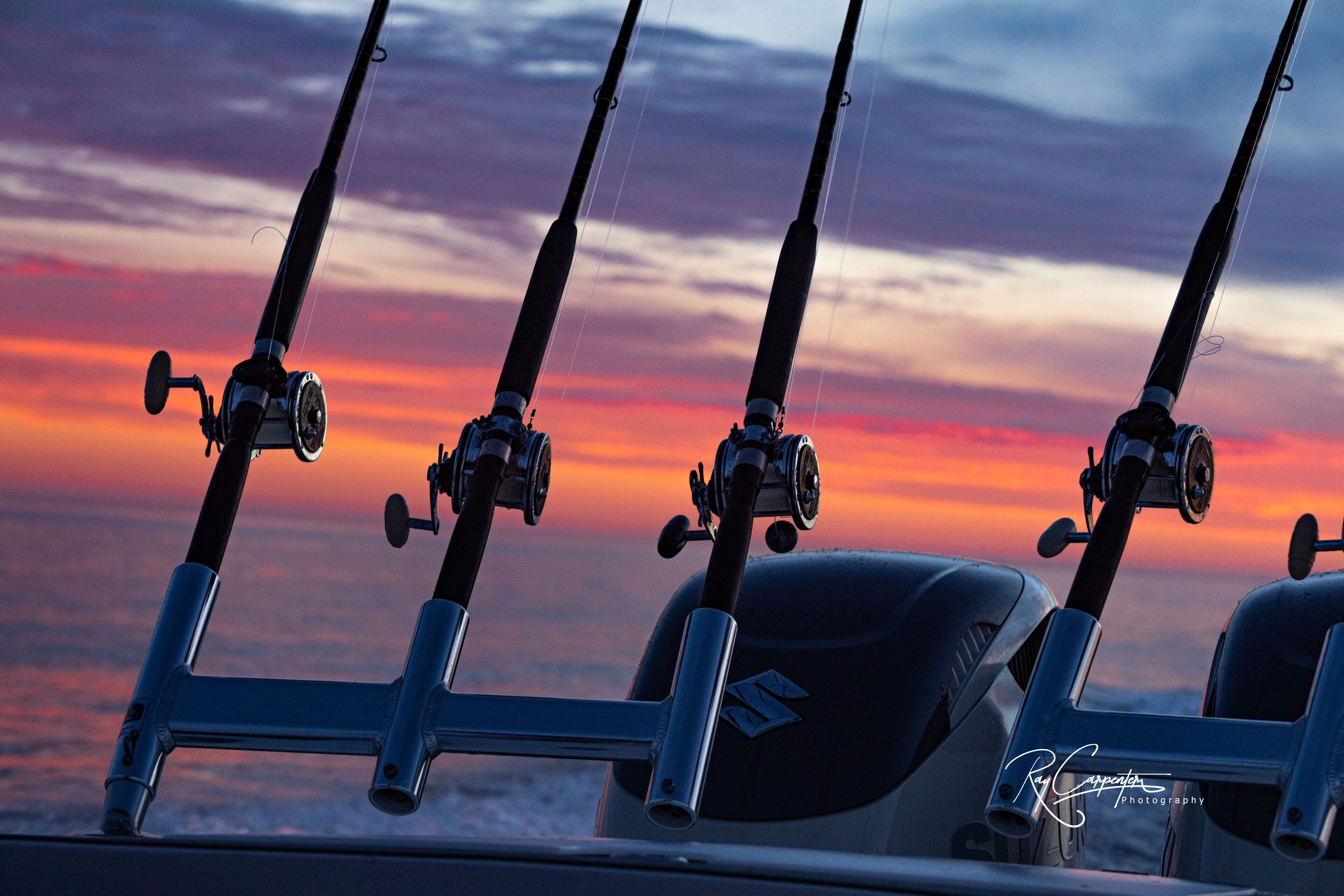 Four fishing rods mounted on a metal stand against a sunset sky.