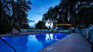 A swimming pool with a covered area, surrounded by trees and a fence.