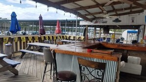 An outdoor bar area with wooden tables and chairs, umbrellas, and a bar counter.