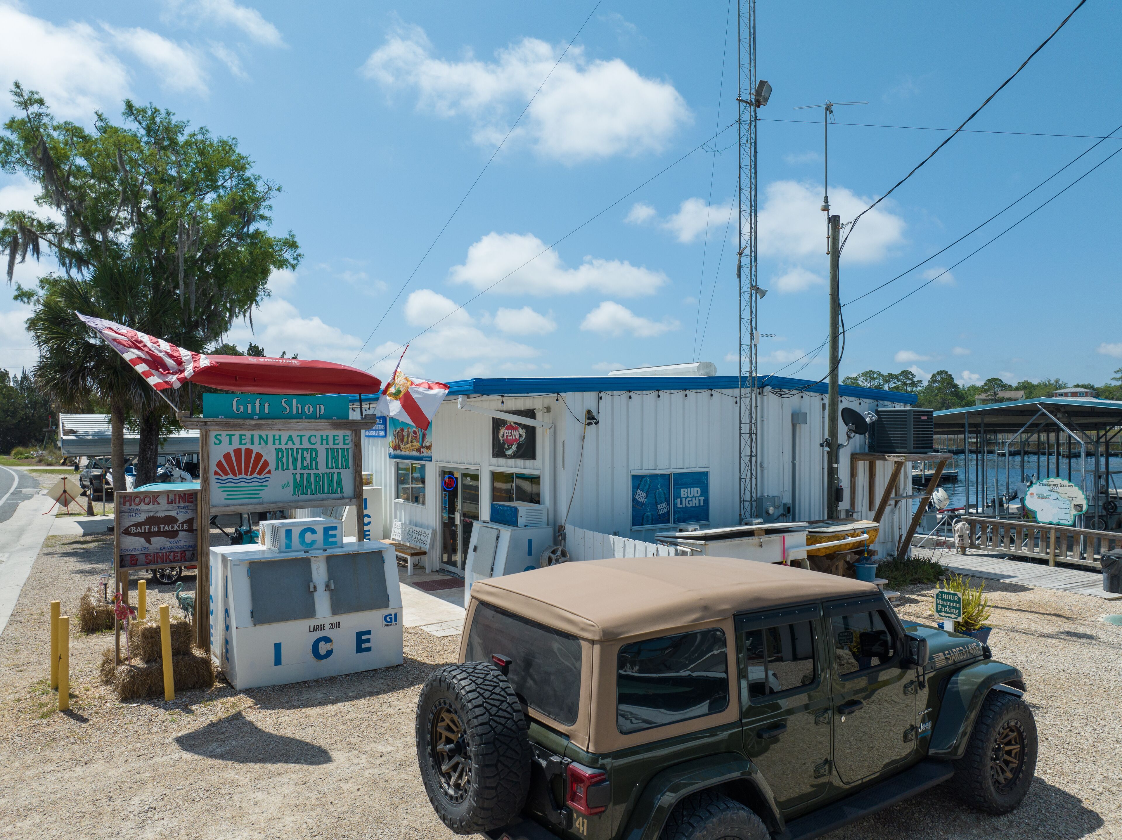 A small roadside establishment with a sign for a gift shop, a river inn, and a marina. A vehicle is parked nearby.