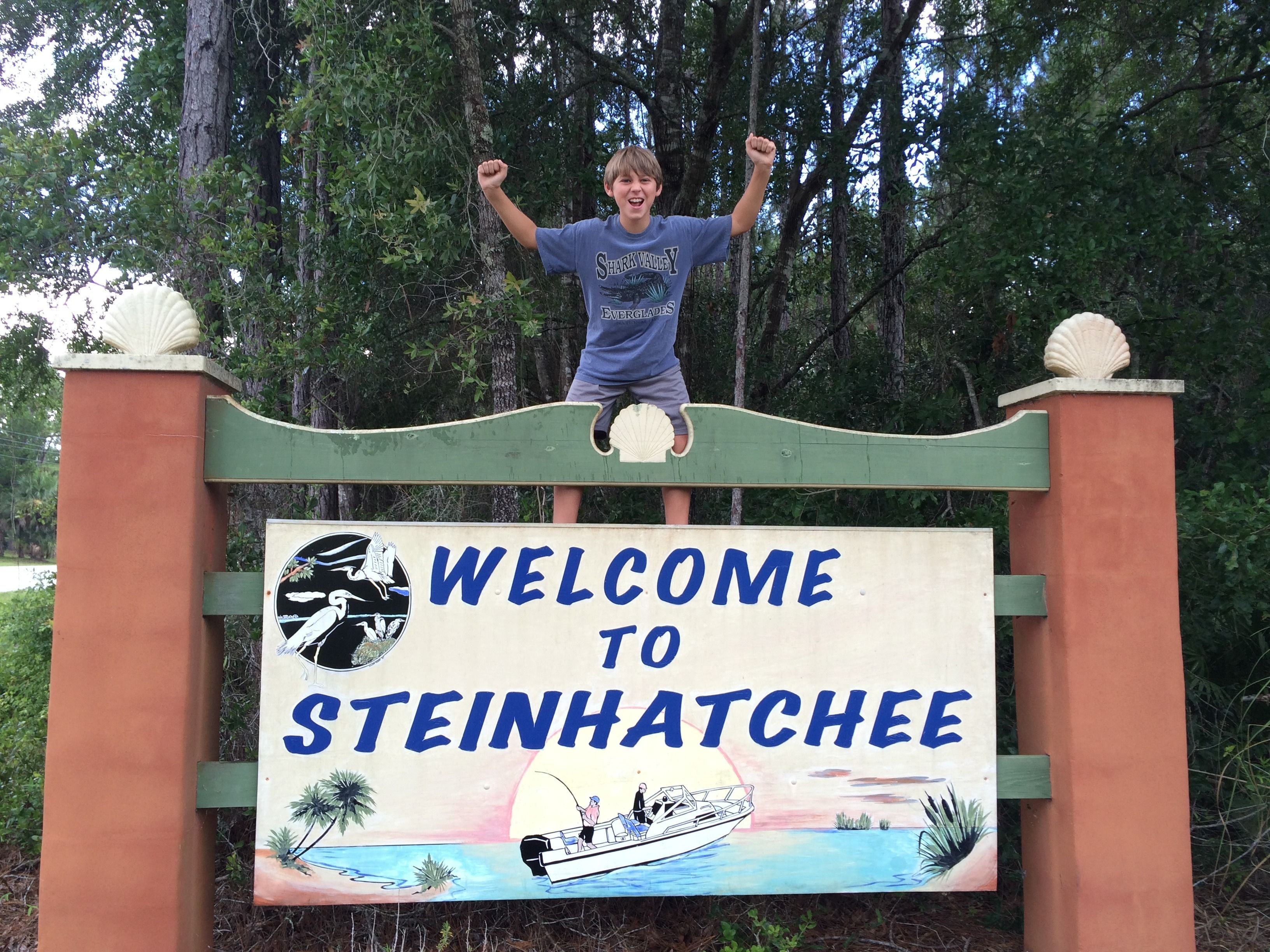 Señal de bienvenida a Steinhatchee con ilustración de un bote y palmeras.